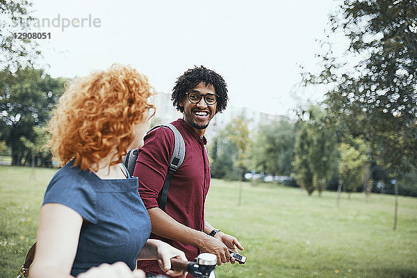 Friends walking in park  talking  woman pushing bicycle