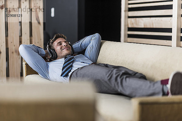 Businessman with headphones lying on couch in office lounge