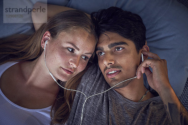 Young couple lying on cushions  sharing earphones  listening music