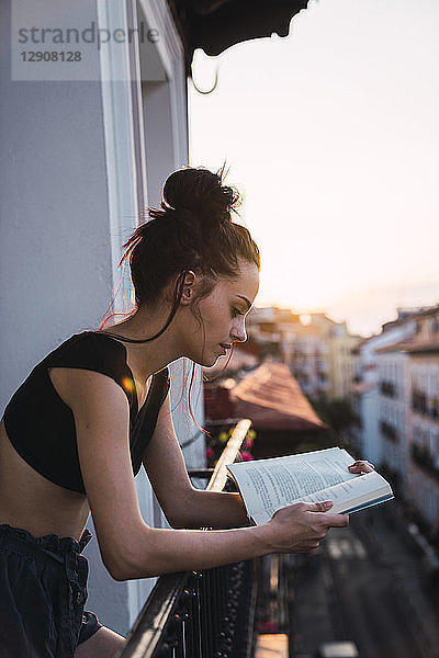 Beautiful young woman on balcony above the city at sunset reading a book