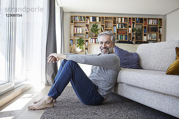Portrait of happy mature man sitting on floor of his living room