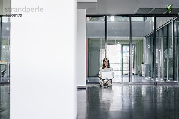 Businesswoman sitting on ground in empty office  using laptop