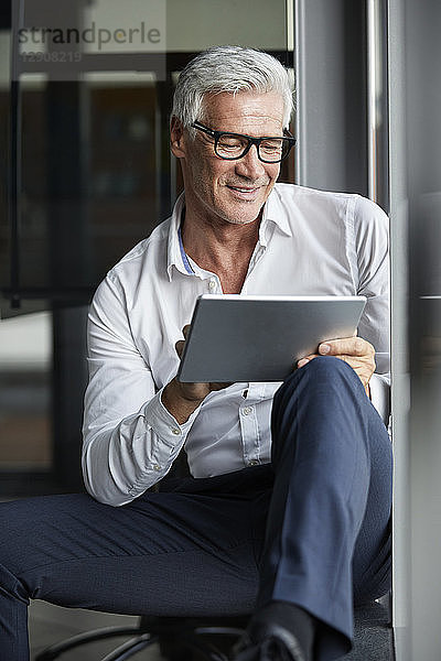 Serene businessman sitting on ground in office  using digital tablet