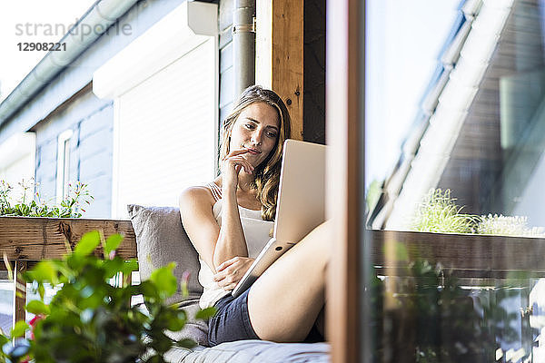 Smiling woman on balcony using laptop