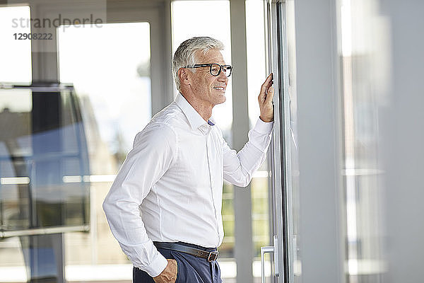 Confident businessman standing in office  looking out of window