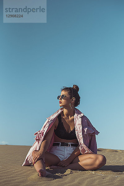 Teenage girl sitting on beach dune against blue sky