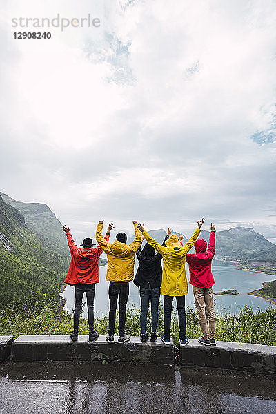 Norway  Senja island  rear view of cheering friends standing on an observation point at the coast