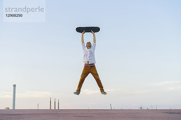 Young man jumping in the air holding a skateboard