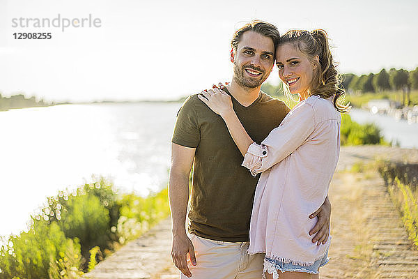 Portrait of smiling affectionate couple standing at the riverside in summer
