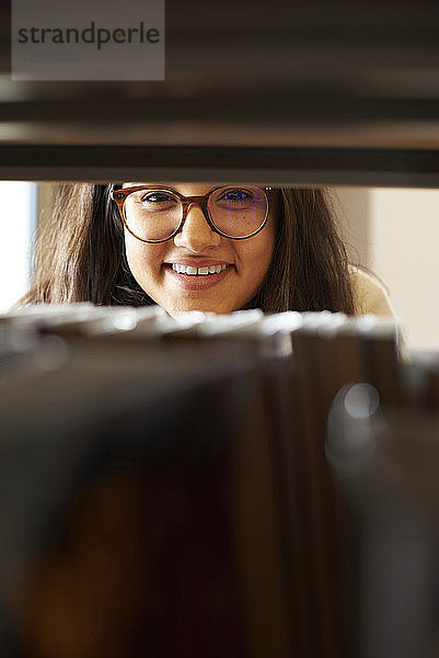 Portrait of smiling young student looking through bookshelf in the library