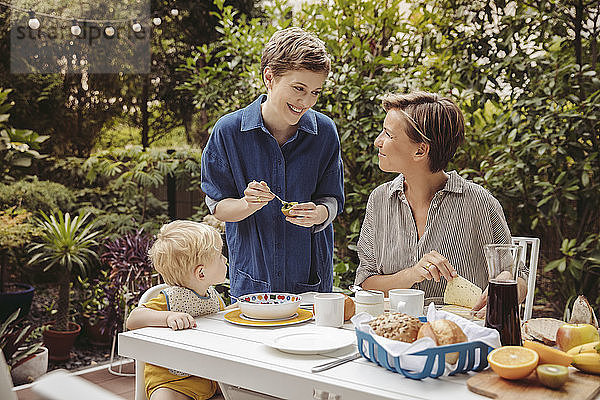 Two happy mothers at breakfast table outdoors with their child