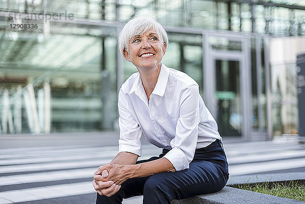 Smiling senior businesswoman sitting outside looking around