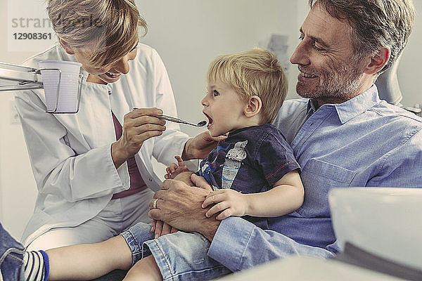 Female dentist examining little boy  sitting on his father's lap