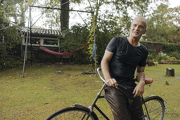 Portrait of mature man with bicycle in summer rain in garden