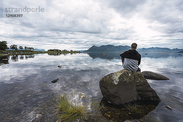 Norway  Senja island  rear view of man sitting on a rock at the coast