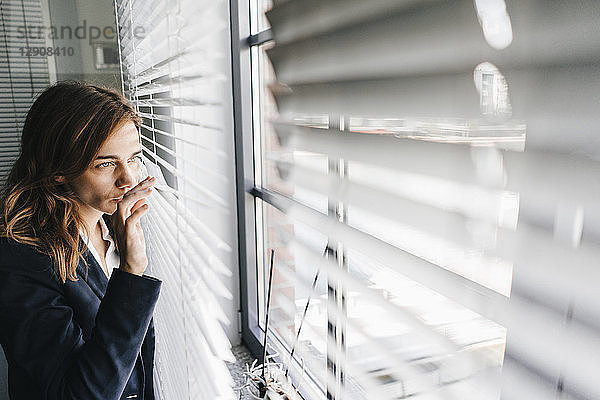 Woman standing by window  spying through blinds