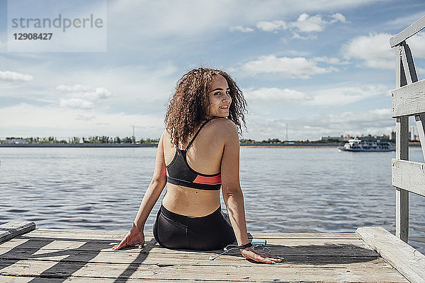 Smiling young athletic woman sitting at the riverside