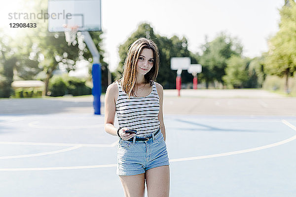 Portrait of young woman on sports ground holding cell phone