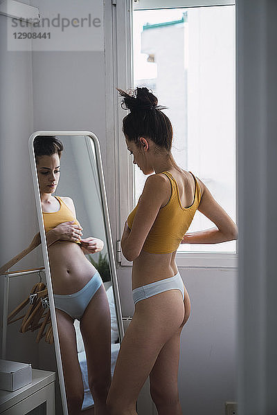 Young woman in underwear at home looking in mirror