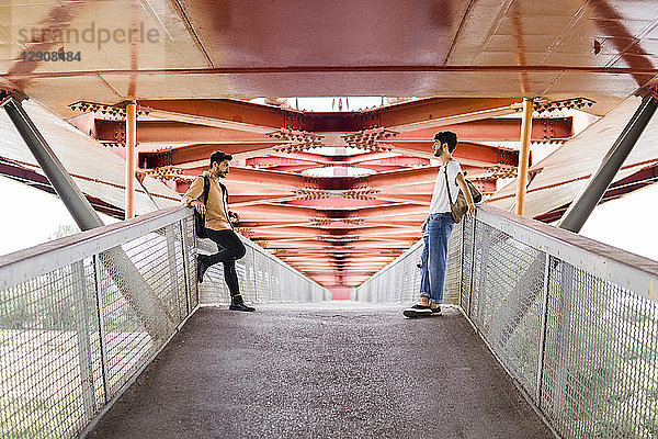 Young gay couple standing on modern footbridge looking at each other