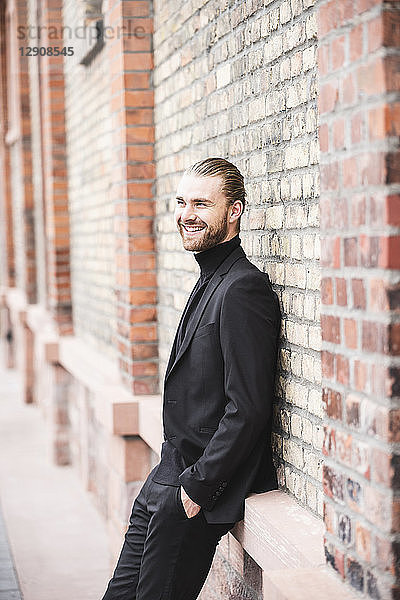 Smiling fashionable young man leaning against brick wall