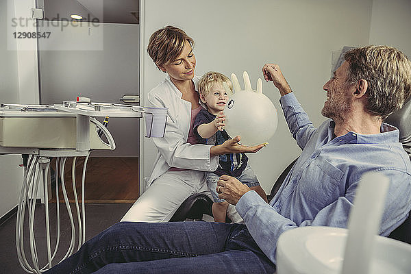 Little boy siting on dentist's lap  playing with a balloon  father smiling