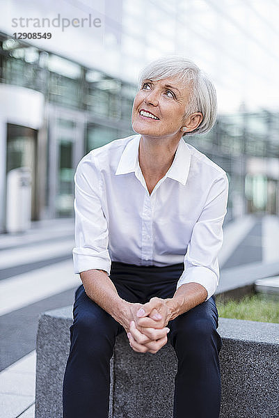 Smiling senior businesswoman sitting outside looking up