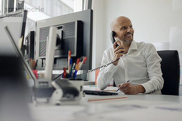 Smiling businessman sitting at his desk  talking on the phone