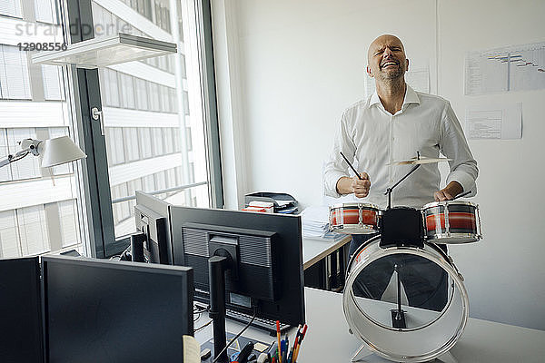 Businessman making noise with drums in his office