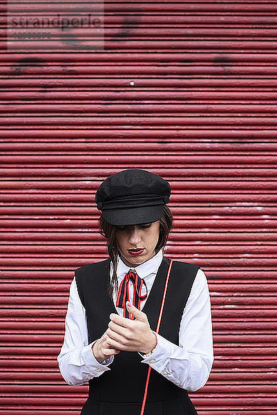 Fashionable woman with red lips wearing black peaked cap standing in front of red roller shutter