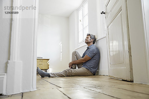 Mature man sitting on floor of his bedroom  daydreaming