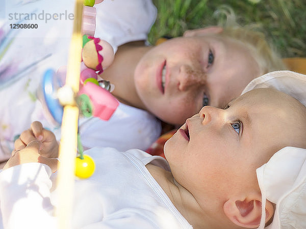 Amazed baby girl lying with her sister on blanket on a meadow