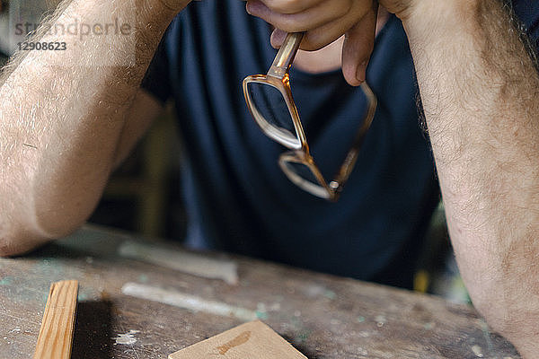 Close-up of man at workbench in workshop holding eyeglasses