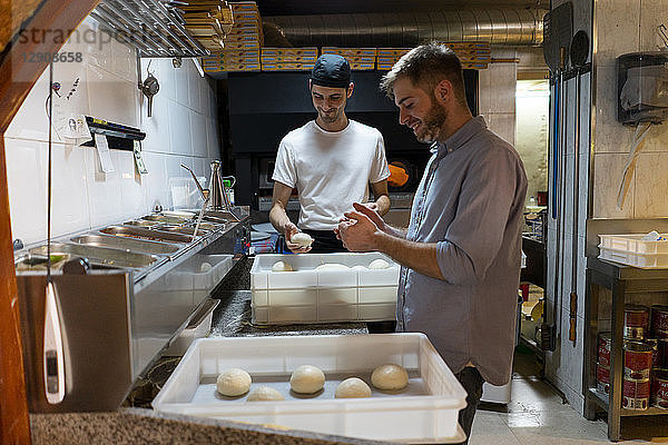 Two men with raw dough in boxes in kitchen of a pizzeria