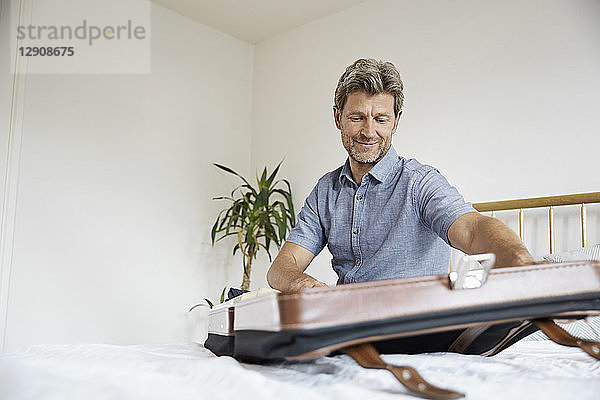 Mature man packing suitcase in bedroom
