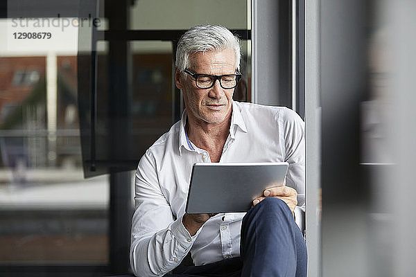 Serene businessman sitting on ground in office  using digital tablet