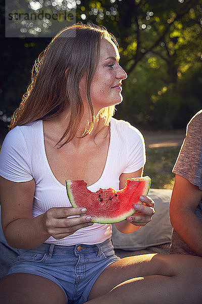 Young couple sitting in park  eating watermelon