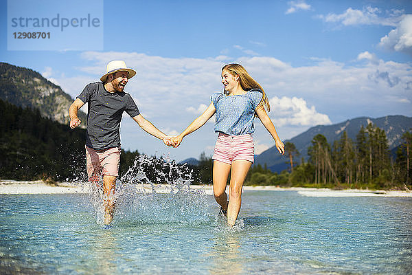 Young couple holding hands and running through water