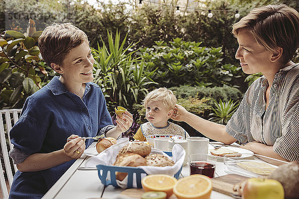 Two happy mothers at breakfast table outdoors with their child