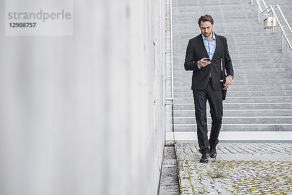 Businessman walking at stairs looking at smartphone