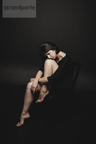 Portrait of woman wearing black sitting in front of black background