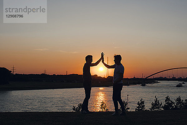 two friends high-fiving at sunset  standing by the river
