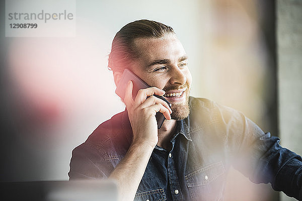 Portrait of smiling young businessman on cell phone in office