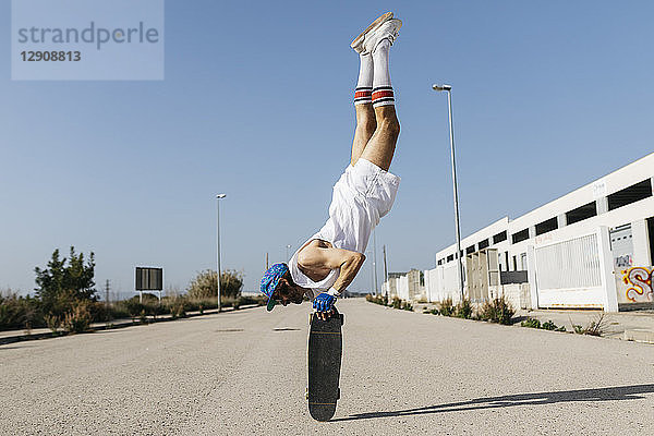 Man in stylish sportive outfit standing on skateboard upside down