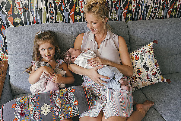 Smiling mother sitting on couch with newborn baby and daughter