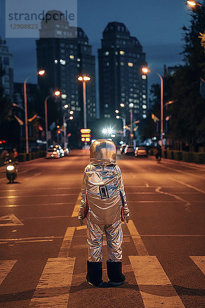 Rear view of spaceman standing on a street in the city at night