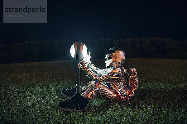 Spaceman sitting on a meadow at night amazed at a lamp