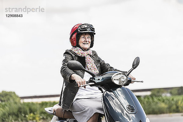 Active senior lady riding motor scooter on the road