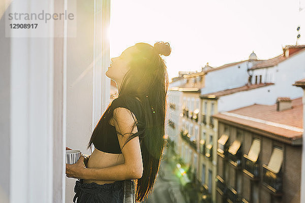 Beautiful young woman on balcony above the city at sunset