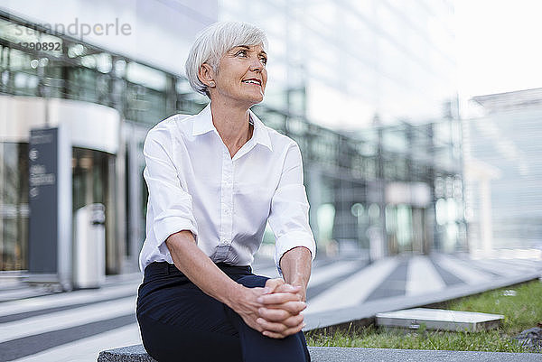 Smiling senior businesswoman sitting outside looking around